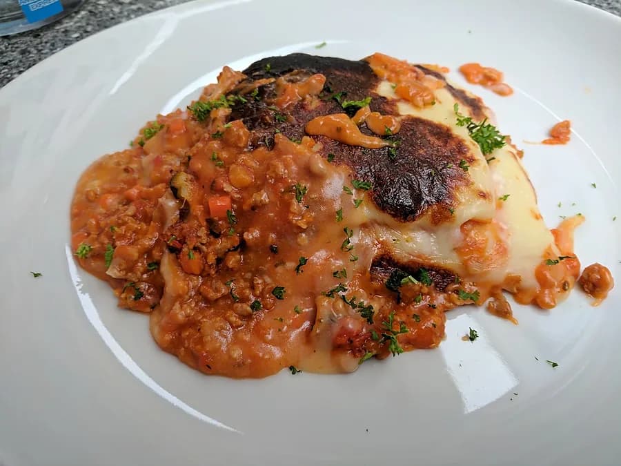 Un plat du jour gratiné du Massala Gourmand, nappé de sa sauce maison, dans une assiette blanche.