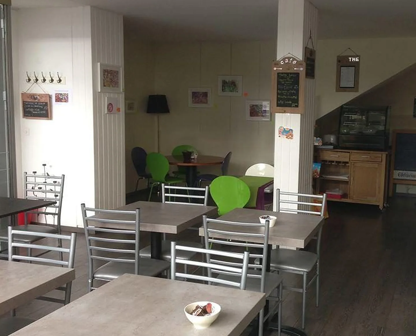 La salle-galerie du Massala Gourmand : tables claires, chaises vertes, œuvres encadrées aux murs et ardoises « café » et « thé », rue des Voisins à Genève.